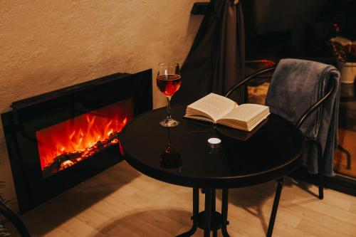 una copa de vino y un libro sobre una mesa junto a la chimenea en Rose Valley Cottage en Ieriķi