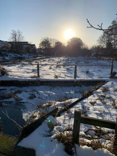 a snow covered field with the sun in the background at The Mill House - Saeby Watermill in Sæby