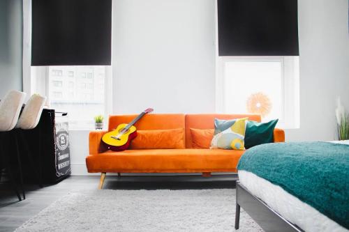 an orange couch in a living room with a guitar at Vibrant Studio Close to Anfield Stadium in Liverpool