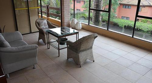 un salon avec une table, des chaises et des fenêtres dans l'établissement Flat Amarilis Riviera de São Lourenço - Flat Lindo com Varanda, à Riviera de São Lourenço