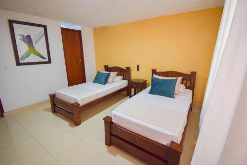 two beds in a room with yellow walls at Hotel Toledo Plaza in Armenia