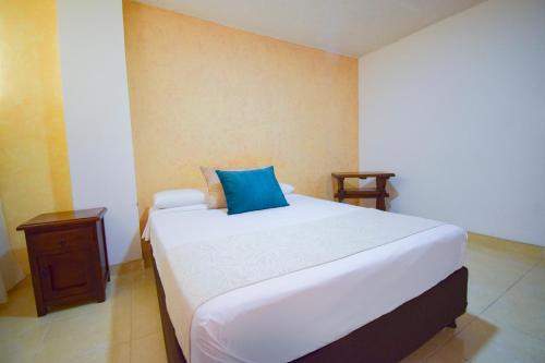 a bedroom with a large white bed with a blue pillow at Hotel Toledo Plaza in Armenia