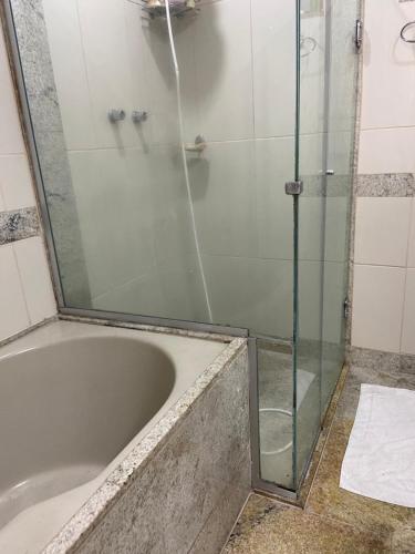 a bathroom with a tub with a glass shower door at Apartamento Praça da Liberdade in Belo Horizonte