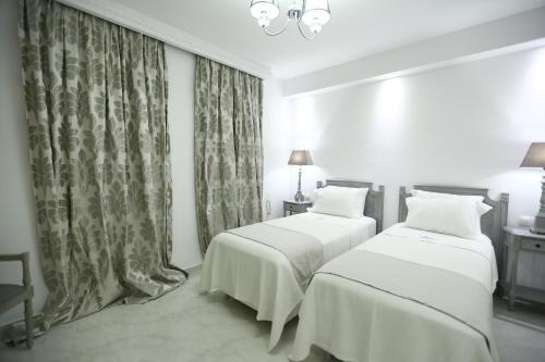 two beds in a white room with curtains at The White Suites in Adamas