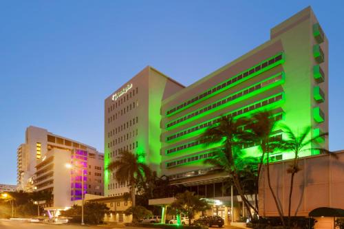 a green building with palm trees in front of it at Holiday Inn Miami Beach-Oceanfront by IHG in Miami Beach