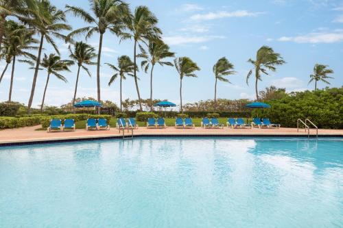 a swimming pool with chairs and umbrellas and palm trees at Holiday Inn Miami Beach-Oceanfront by IHG in Miami Beach