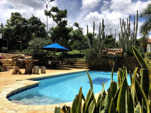 a blue swimming pool with a blue umbrella and cactus at Finca Hacienda Casa Prada in Bucaramanga