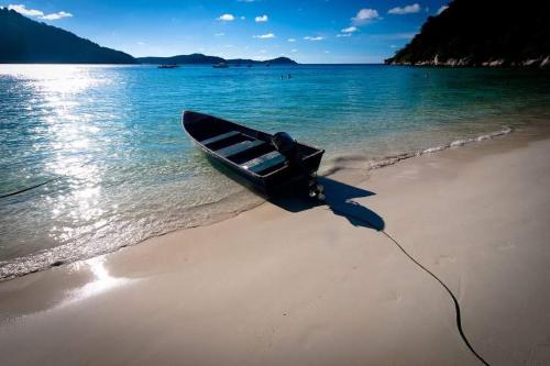a boat sitting on a beach next to the water at Matahari Chalet Long Beach Perhentian Island in Perhentian Islands