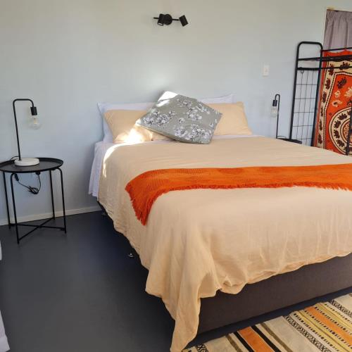 Un dormitorio con una cama grande con una manta naranja. en Mountain View Studio, en Raglan
