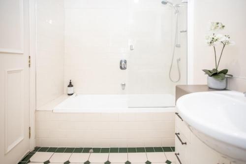 a white bathroom with a white tub and a green tile floor at Historic Apartment - Cathedral Square CBD in Christchurch