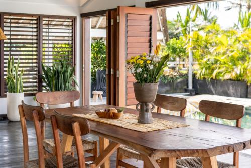 a wooden table with chairs and a vase with flowers on it at Bombora Medewi in Pulukan