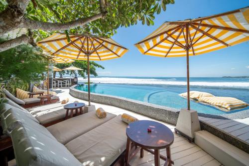 a resort patio with a pool and tables and umbrellas at Bombora Medewi in Pulukan