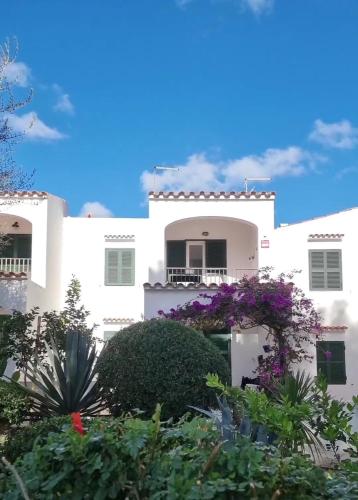 a white building with purple flowers in front of it at HOLIDAYS MENORCA Cala Galdana in Cala Galdana