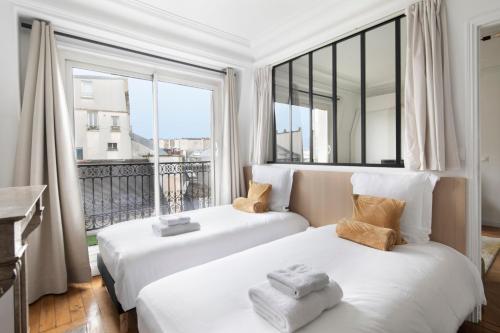 two beds in a room with a large window at Appartement Vertus in Paris