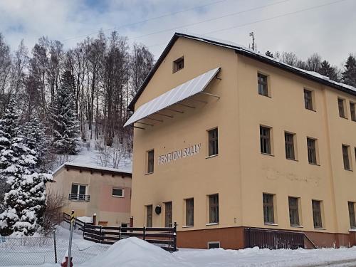 un edificio con un cartello sopra nella neve di Penzion Sally a Albrechtice v Jizerských horách