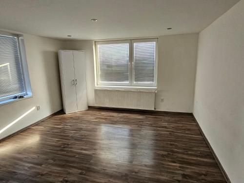 an empty living room with two windows and wooden floors at MINOS in Košice