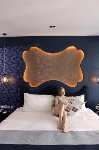 a woman sitting on a bed reading a newspaper at Avista Grande Phuket Karon - MGallery in Karon Beach