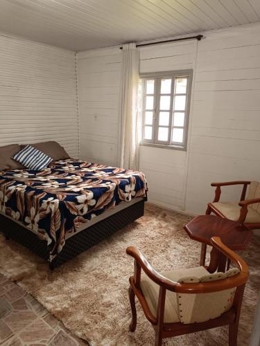 a bedroom with a bed and a chair and a window at Casa Amarela in Lages