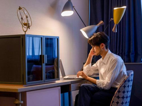 un homme assis à un bureau avec un ordinateur portable dans l'établissement Mercure Tokyo Ginza, à Tokyo