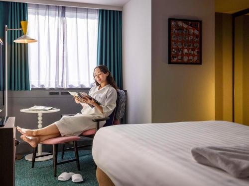 une femme assise sur une chaise dans une chambre d'hôtel dans l'établissement Mercure Tokyo Ginza, à Tokyo