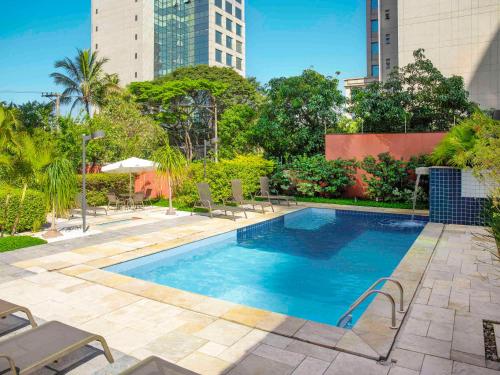 a swimming pool with chairs and trees and buildings at Mercure Sao Paulo Berrini in Sao Paulo