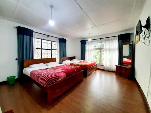 two beds in a large room with wood floors and windows at Sapu's Mountain breeze Nuwara Eliya in Nuwara Eliya