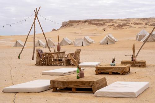 un campamento desierto con mesas, sillas y tiendas de campaña en Tzila Camp, en El Fayum