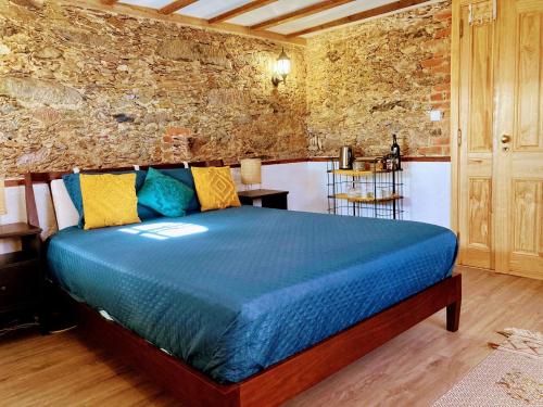 a bedroom with a bed with blue sheets and a stone wall at A Casa Amarela Guest room in São Martinho da Cortiça