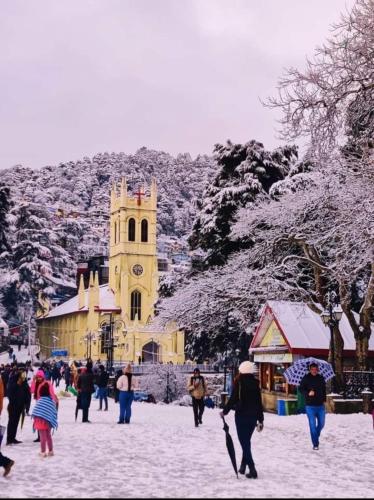 people walking in the snow in front of a building with a clock tower at ASTON HOME STAY in Chhota Simla