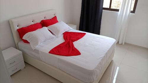 a bedroom with a white bed with red pillows at T2 no Recanto d' fonte francês in Mindelo