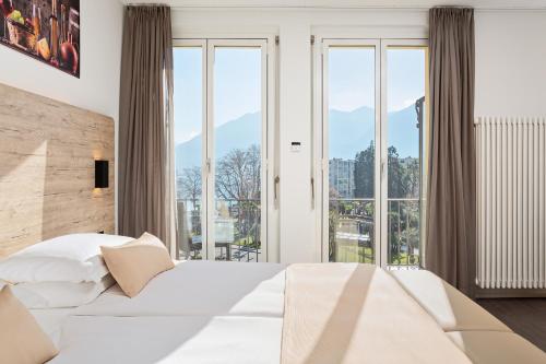 Schlafzimmer mit einem weißen Bett und großen Fenstern in der Unterkunft Hotel Du Lac in Locarno