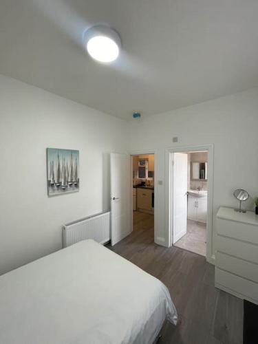 a white bedroom with a bed and a kitchen at Pearl- Deluxe London Studio Flat in South Norwood