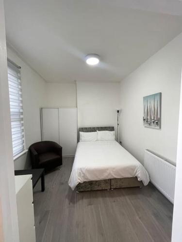 a white bedroom with a bed and a chair at Pearl- Deluxe London Studio Flat in South Norwood