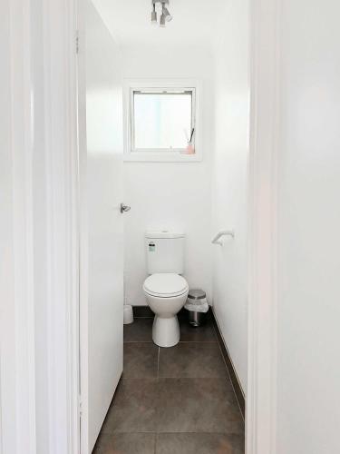 a white bathroom with a toilet and a window at Serene 4Bed2Bath House w Parking Near Mornington Peninsula in Frankston