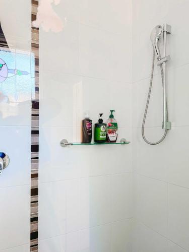 a white bathroom with a shower and two bottles on a shelf at Serene 4Bed2Bath House w Parking Near Mornington Peninsula in Frankston