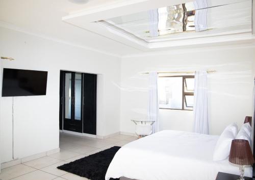 a white bedroom with a bed and a tv at AZALEA LODGE in Midrand