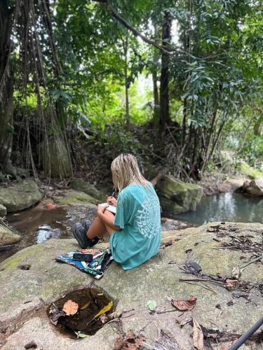 a woman sitting on a rock next to a river at SZ Samui Glamping in Ban Sa Ket