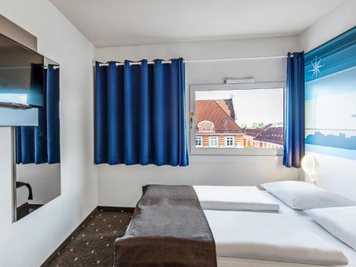 a bedroom with a bed and a window with blue curtains at B&B Hotel Hamburg-Altona in Hamburg