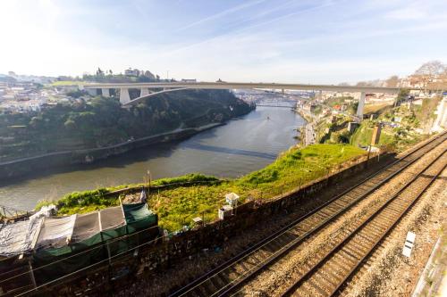 ein Zug auf Gleisen neben einem Fluss mit einer Brücke in der Unterkunft Sao Victor Suites in Porto
