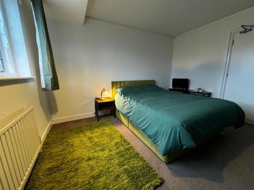 a bedroom with a bed with a green comforter and a rug at The Airman in Feltham