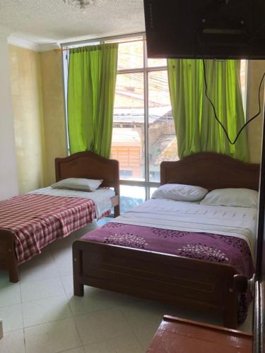 two beds in a room with green curtains and a window at Hotel SION in Pitalito