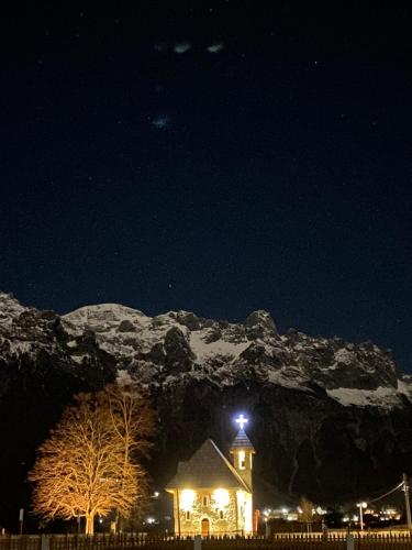 a building with a clock tower in front of a mountain at Guesthouse Prrockaj Theth in Theth