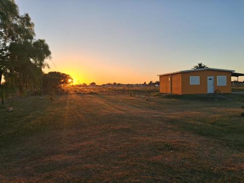 Ein Haus auf einem Feld mit Sonnenuntergang im Hintergrund in der Unterkunft Estadía Nuestro Sueño in Colonia del Sacramento