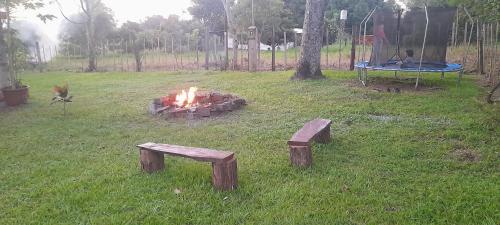 eine Feuerstelle in einem Hof mit zwei Bänken und einem Trampolin in der Unterkunft Cabaña Don floricel in Santa Ana