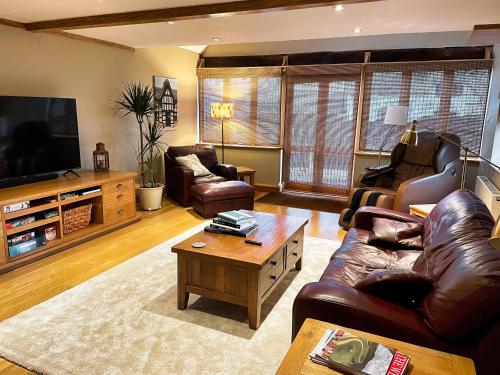 a living room with leather furniture and a flat screen tv at Guest House gem in Wickhamford, near Broadway in Badsey