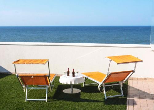 two chairs and a table on a lawn with the ocean at Hotel Harmony in Rimini