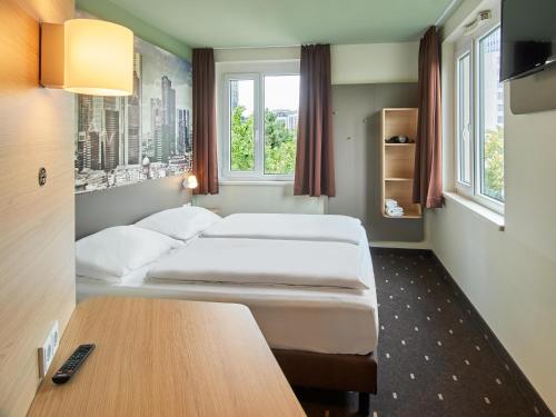 フランクフルト・アム・マインにあるB ＆ B ホテル フランクフルト ウエストのベッド2台、テーブル、窓2つが備わる客室です。