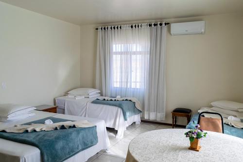 a room with three beds and a table and a window at HOTEL TAIÓ in Taió