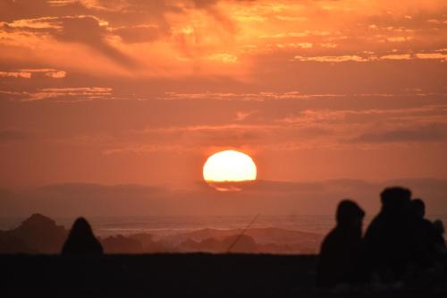 a group of people sitting on the beach watching the sunset at SURFHOUSE Pichilemu in Pichilemu
