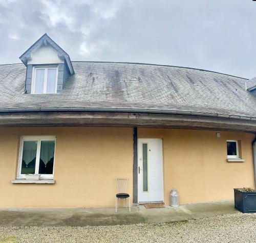 une maison jaune avec une porte blanche et une chaise dans l'établissement Le Clos De La Vallée, à Bellengreville